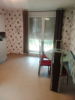A room with a dining table and chairs, a glass-top table, a sliding glass door leading to an outdoor area, and patterned wallpaper.