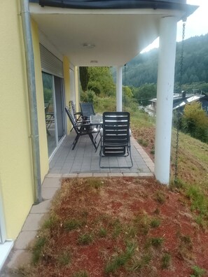Un espace extérieur aménagé, abrité et doté d’une table et de chaises, d’une porte-fenêtre coulissante et d’une vue sur le paysage environnant.