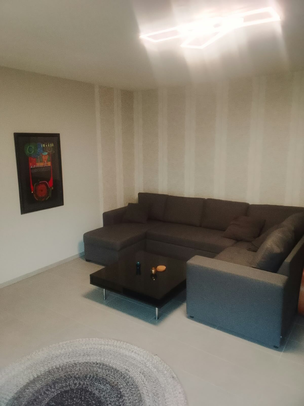 Ein Wohnzimmer mit einem Ecksofa, einem Couchtisch und einem an der Wand befestigten Kunstwerk.
