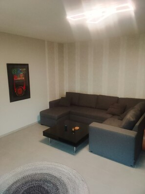 A living room with a sectional sofa, a coffee table, and a wall-mounted artwork.