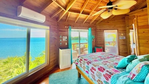 Eine Holzhütte mit Bett, Deckenventilator und Blick auf den Ozean.
