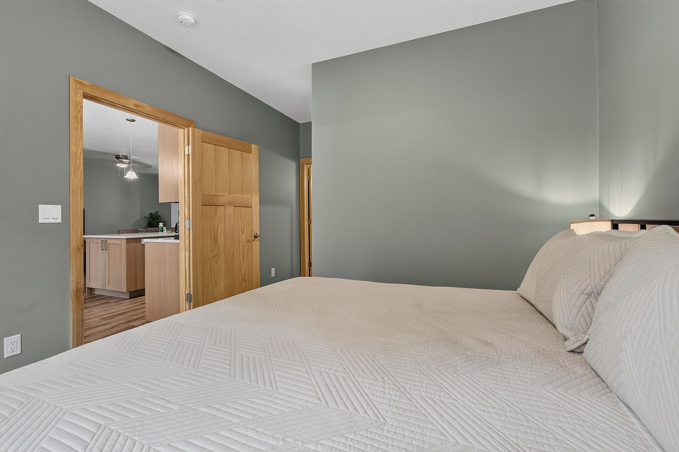Une chambre avec un grand lit, une porte en bois et, au fond, un coin cuisine.