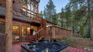 A wooden cabin with a hot tub on a deck, surrounded by trees. - 82 Lenawee Lane (Keystone)