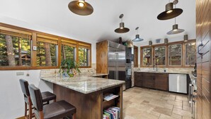 A modern kitchen with a large island, wooden cabinets, stainless steel appliances, and large windows offering a view of the outdoors. - 82 Lenawee Lane (Keystone)