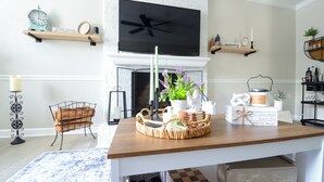 A living room with a wooden coffee table, a fireplace, a television, and various decorative items. - Premier Homestead Retreat on 1.5 Acres: Pets, Spa, Firepit, Chickens, King, Gym (Wake Forest)