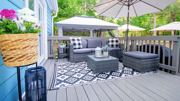 A covered outdoor seating area with wicker furniture, a patterned rug, and umbrellas. - Premier Homestead Retreat on 1.5 Acres: Pets, Spa, Firepit, Chickens, King, Gym (Wake Forest)