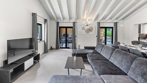 Een moderne woonkamer met een flatscreen-tv, een grijze bank en een eethoek met een tafel gedekt voor twee personen.