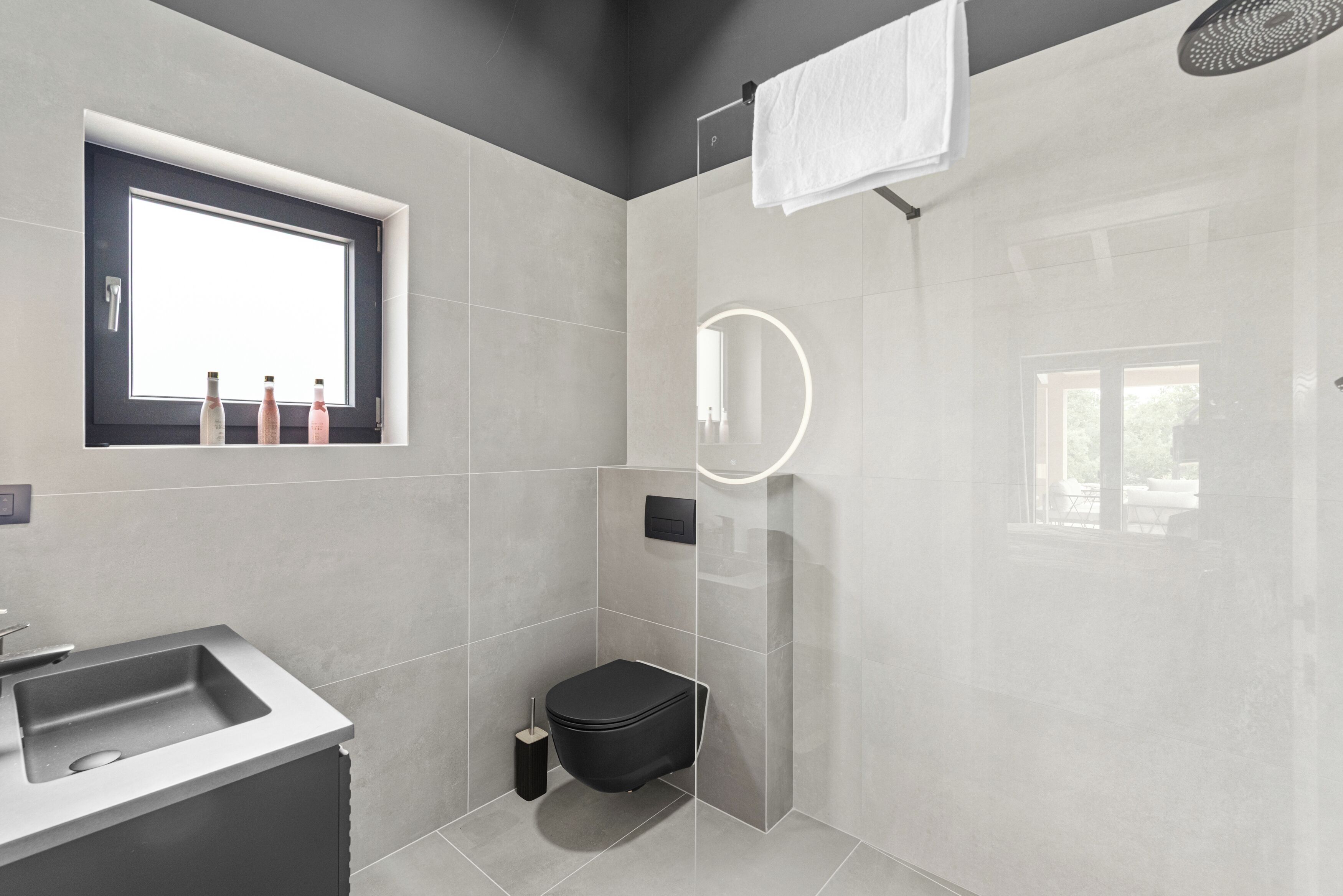 Ein modernes Badezimmer mit großem Fenster, integriertem Waschbecken, Toilette und Duschbereich.