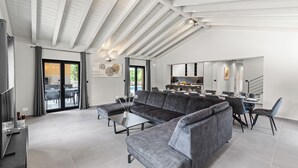 Een ruime woonkamer met een grote hoekbank, een eettafel met stoelen, en een keuken op de achtergrond.