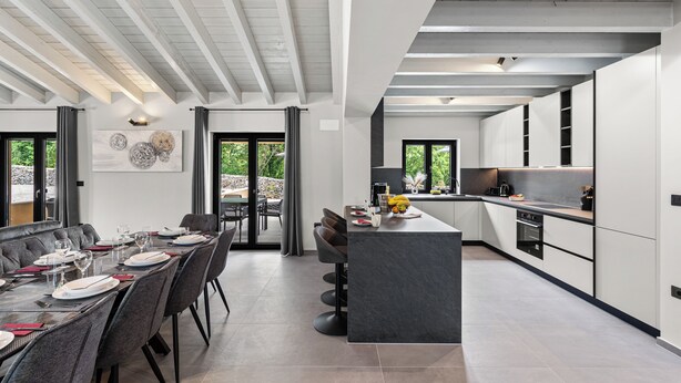 Een moderne keuken met een centraal eiland, donkere kasten en een eethoek met een lange tafel en stoelen.