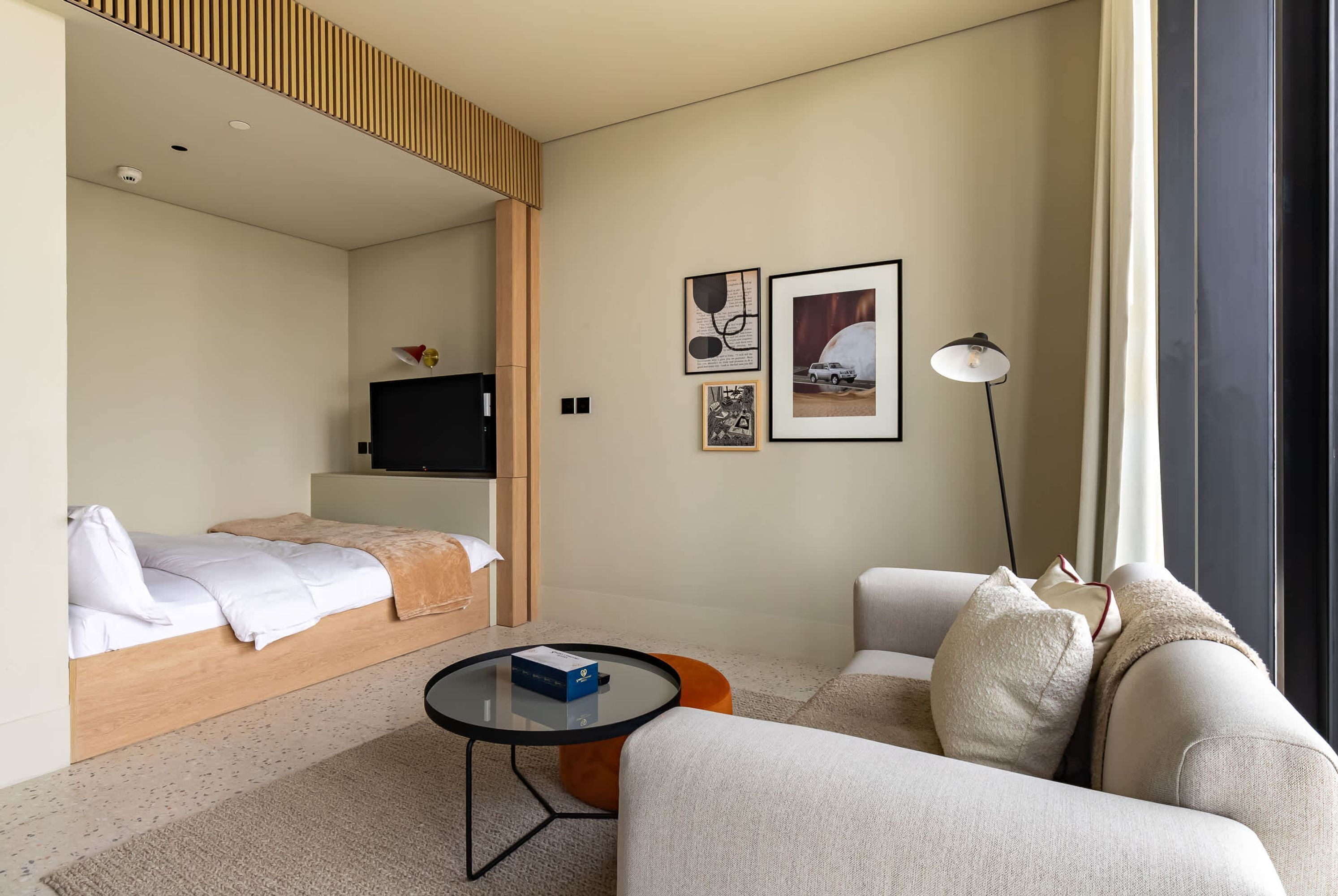 A modern hotel room with a bed, a sofa, a coffee table, and artwork on the walls.
