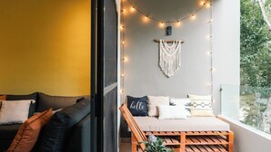A cozy balcony with a wooden bench, string lights, macrame wall hanging, and a potted plant. - Peace Family Vacation Home, Swimming Pool, Barbecue Grills and Gym (Playa del Carmen)