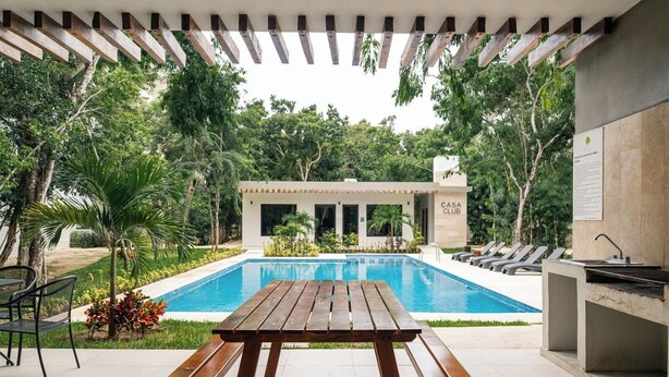 A pool area with a wooden table and lounge chairs, surrounded by lush greenery and a building labeled "CASA CLUB". - Peace Family Vacation Home, Swimming Pool, Barbecue Grills and Gym (Playa del Carmen)