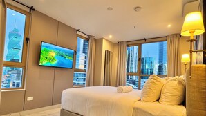 Habitación de hotel con una cama grande, un televisor de pantalla plana montado en la pared y vistas de la ciudad a través de las ventanas.