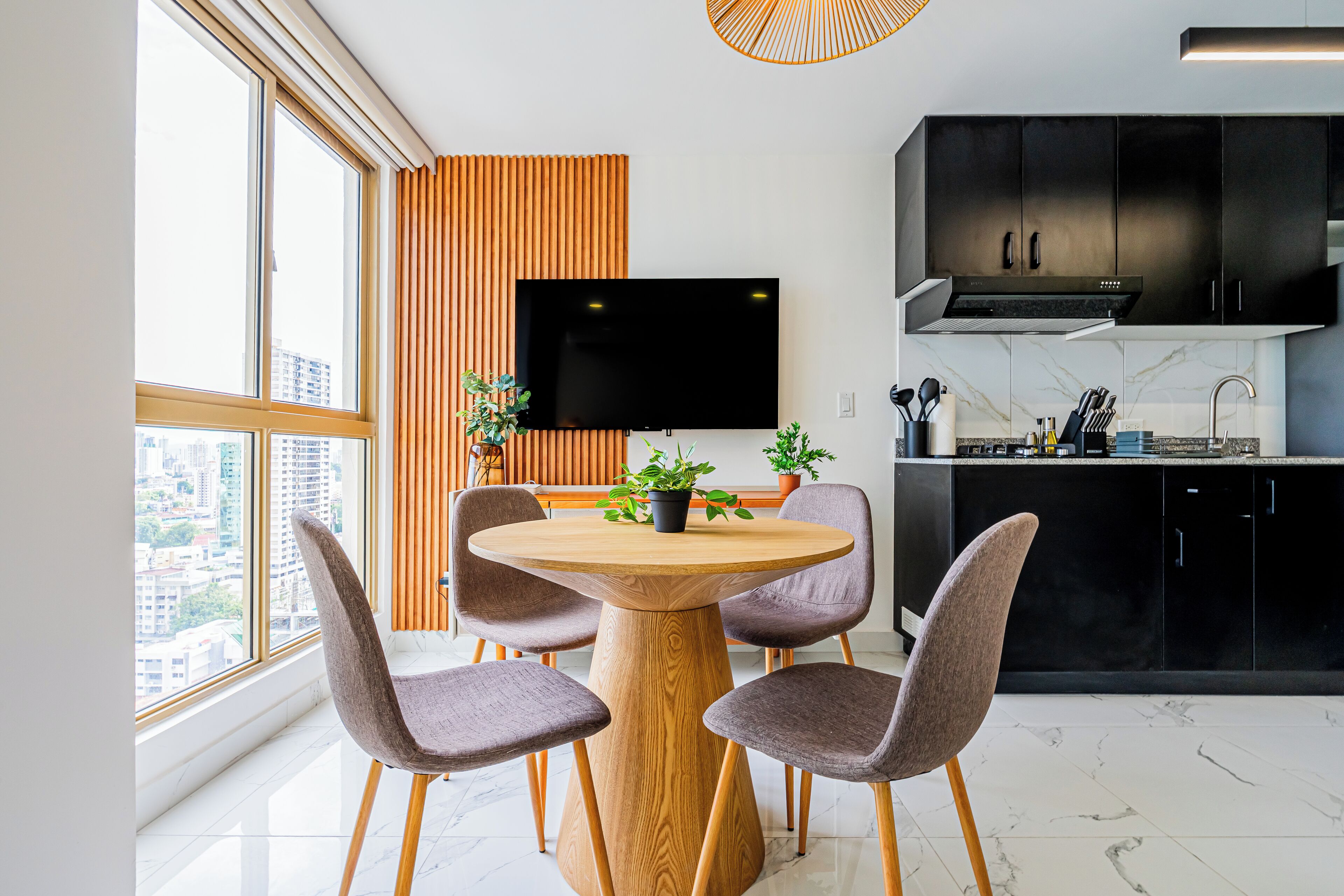 Une cuisine moderne avec une table ronde en bois, quatre chaises, un téléviseur à écran plat et des meubles de rangement noirs.