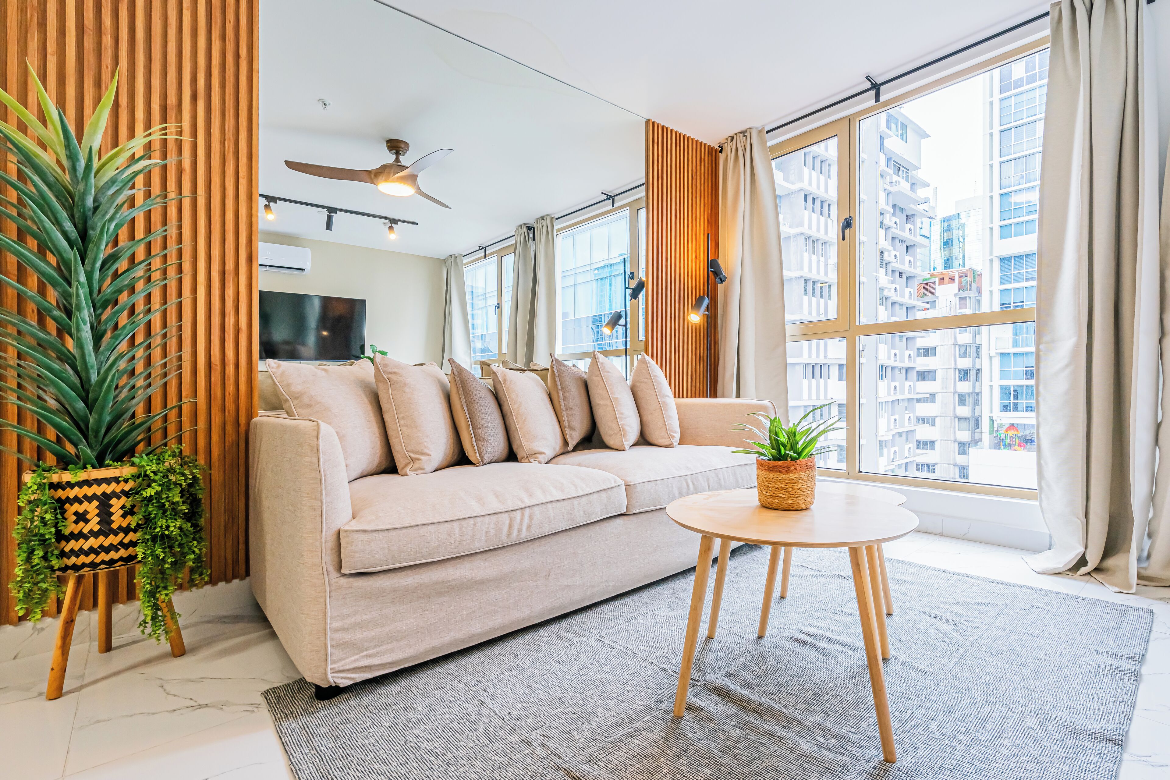 A modern living room with a beige sofa, a round wooden coffee table, and a large window with curtains.