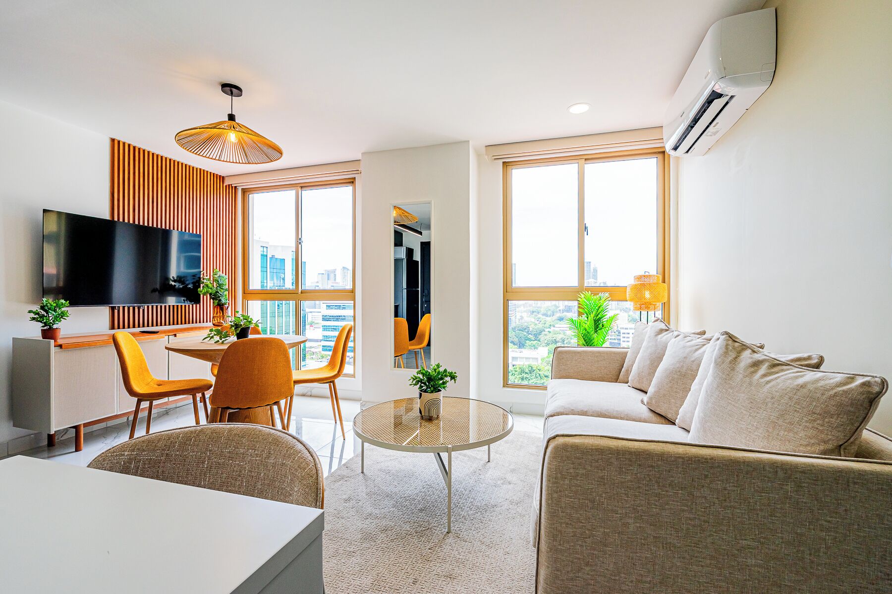 A modern living room with a sofa, a dining table, chairs, a TV, and a large window with a city view.