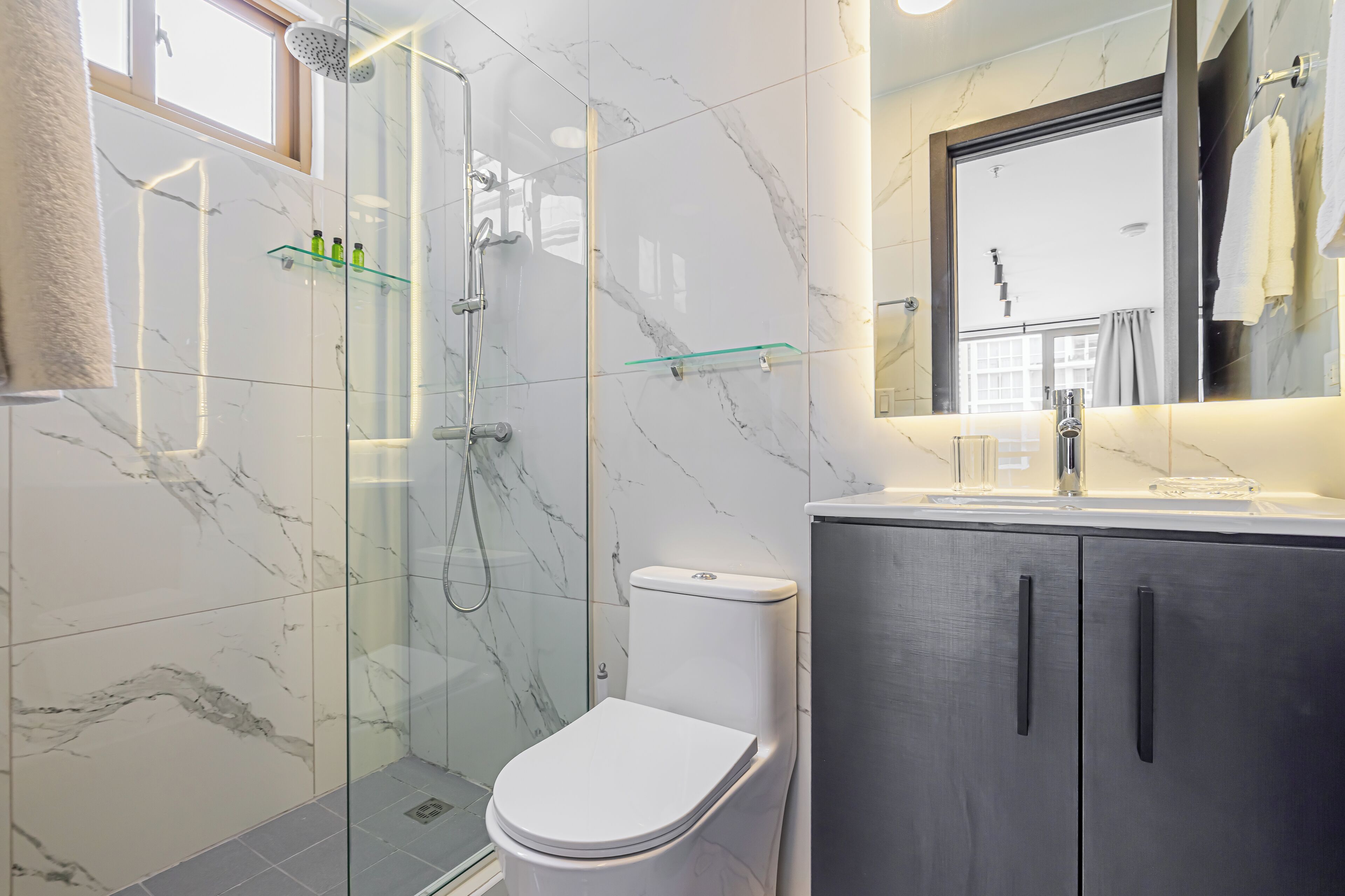 Un bagno moderno con doccia vetrata, un WC bianco e un mobile lavabo scuro con uno specchio.