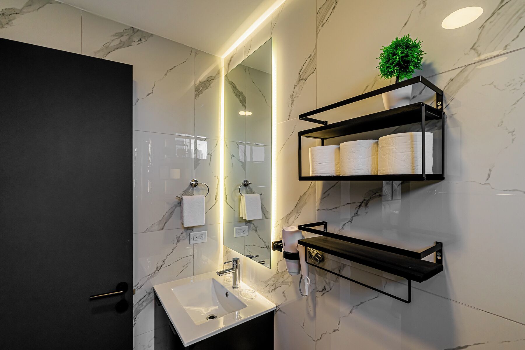 A modern bathroom with a marble backsplash, a large mirror, a sink, and built-in towel racks.