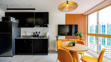 A modern kitchen with black cabinets, a marble backsplash, and a built-in oven. There's a dining area with a round wooden table and yellow chairs, and a large window offering a city view.