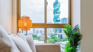 Una habitación con vistas a un edificio moderno, una ventana con una lámpara tejida y una planta en maceta.