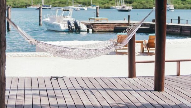 Een houten terras met een hangmat, een zwembad en uitzicht op boten in een jachthaven.
