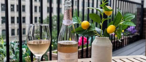 A table with a bottle of Brut Rose wine, a glass of wine, and a bowl of dried fruits on a balcony with a city view.