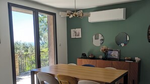 Zona pranzo con tavolo in legno, quattro sedie, ventilatore a soffitto e vista su un balcone esterno attraverso una porta in vetro.