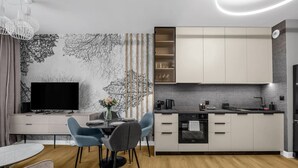 Una cocina moderna con horno empotrado, un comedor con mesa y sillas, y un televisor de pantalla plana sobre un mueble blanco.
