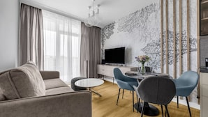 Una sala de estar moderna con sofá, mesa de comedor, sillas, televisor y un adornado muro.