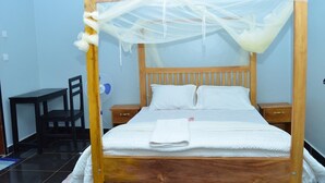 A wooden bed with a canopy, white pillows, and a bedside table. - Kamfart Safari Lodge (Jinja)