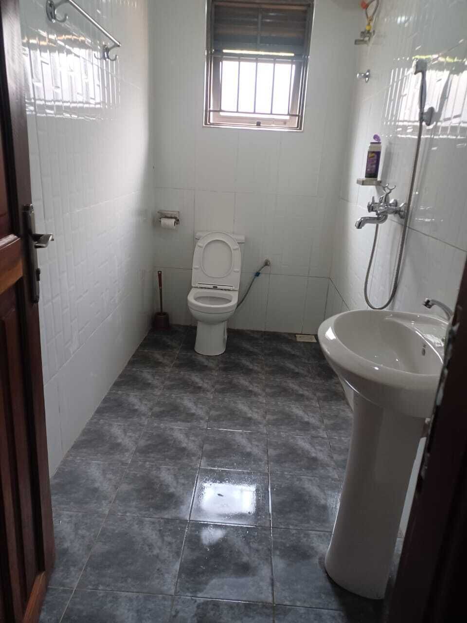 A bathroom with a toilet, sink, shower, and a window.