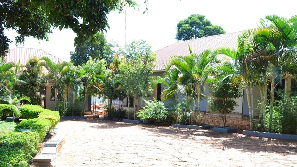 A courtyard with a stone-paved area, surrounded by lush greenery and palm trees, leading to a building with a tiled roof. - Kamfart Safari Lodge (Jinja)