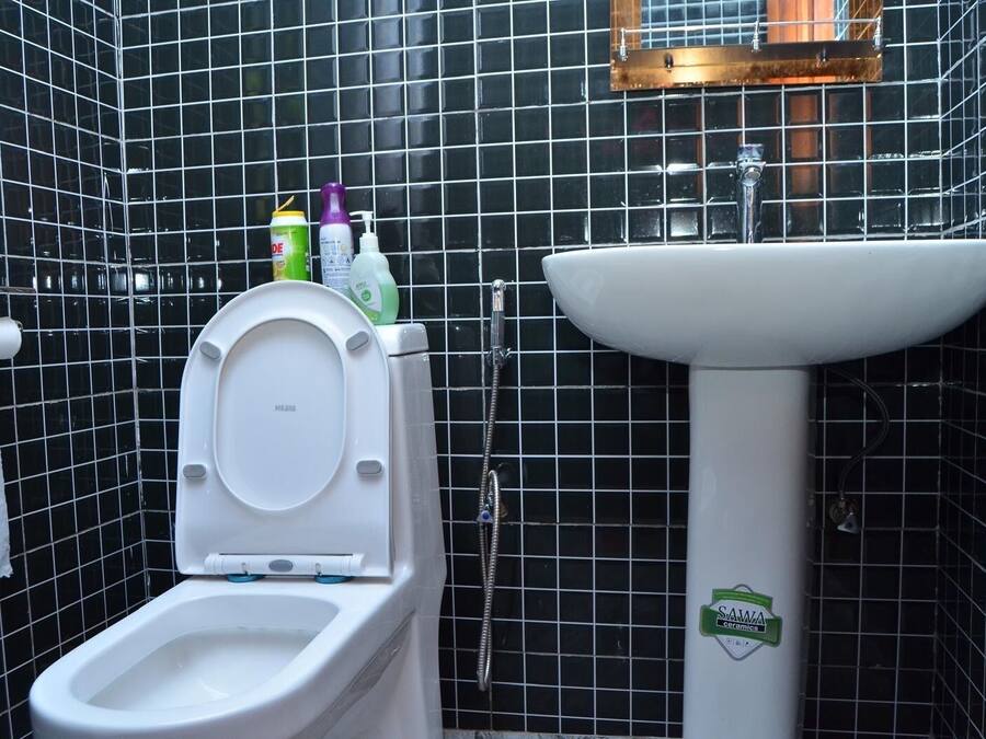 Un baño con inodoro, lavamanos y paredes con azulejos negros.