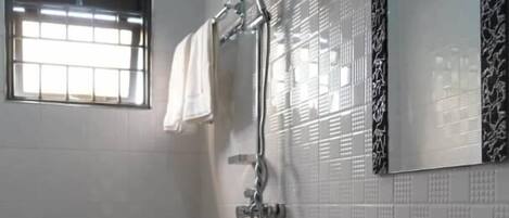 A bathroom with a toilet, sink, shower, and a window with blinds.