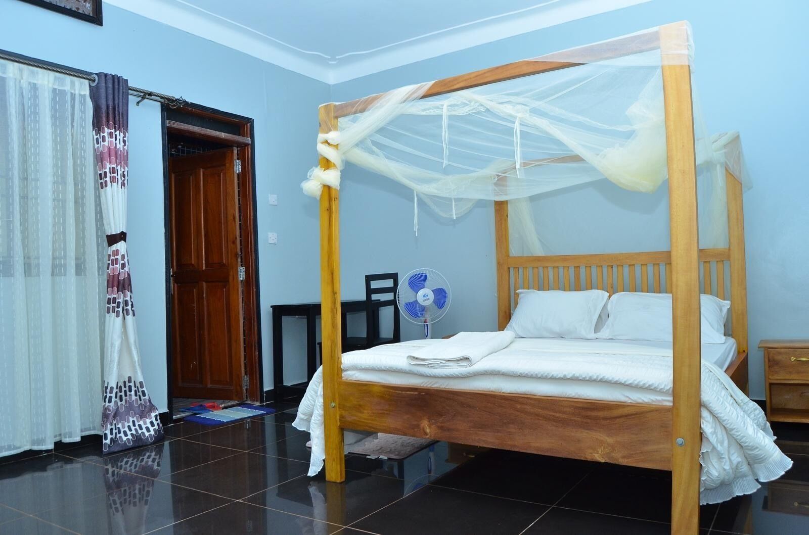 A room with a wooden four-poster bed, a ceiling fan, and a door.