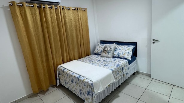 A bedroom with a bed, curtains, an air conditioning unit, and a door. - Private room in Balneário Camboriú (Centro Balneário Camboriú)