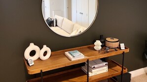 Une console en bois surmontée d’un miroir, un vase blanc, un livre et un petit haut-parleur.