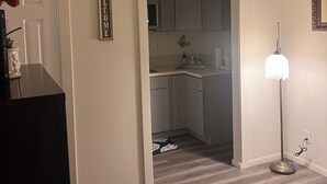 A hallway leading to a kitchen with white cabinets and a dark wood floor. - Detached Casita  studio charming Perris (Perris)