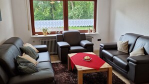 A modern living room with two leather sofas, a wooden coffee table, and a large window with a view of greenery. - Bright vacation apartment in East Frisia with large garden and terrace (Friedeburg)