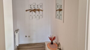 A hallway with a white radiator, a wooden floor, a white console table with a vase, and a wall-mounted mirror. - Bright vacation apartment in East Frisia with large garden and terrace (Friedeburg)