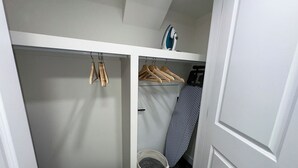 Een kast met houten kleerhangers, een strijkplank en een wasmand.