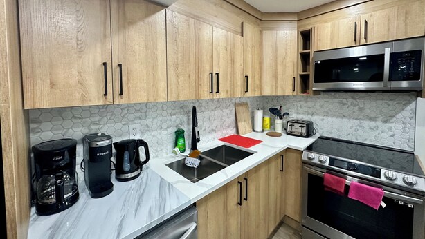 Een keuken met houten kastjes, een magnetron, een fornuis en een koffiezetapparaat.