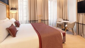 Une chambre d’hôtel avec un grand lit, un bureau, deux chaises, une télévision et des rideaux.
