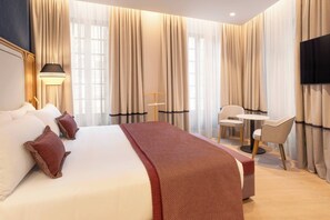 Une chambre d’hôtel avec un grand lit, un bureau, deux chaises, une télévision et des rideaux.
