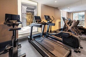 Une salle de sport équipée de tapis de course, de vélos elliptiques et d’haltères.