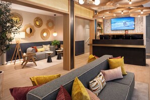 A modern hotel lobby with a reception desk, seating area, and decorative wall mirrors.