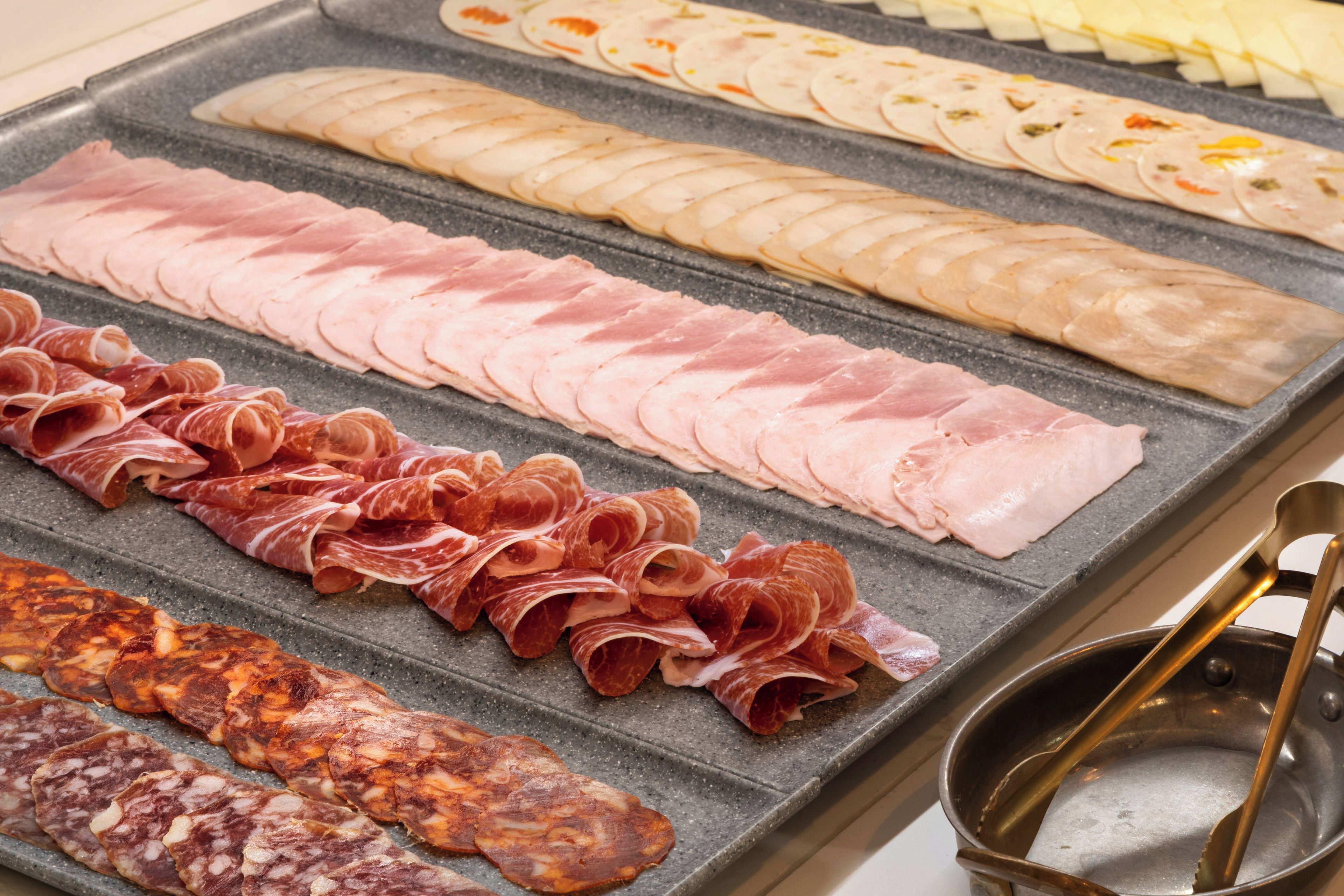 A variety of sliced meats on a grill.