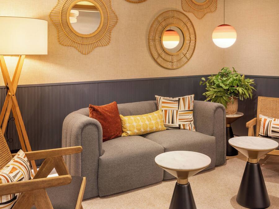 A modern lounge area with a grey sofa, patterned cushions, a wooden chair, a small table, and decorative mirrors on the wall.