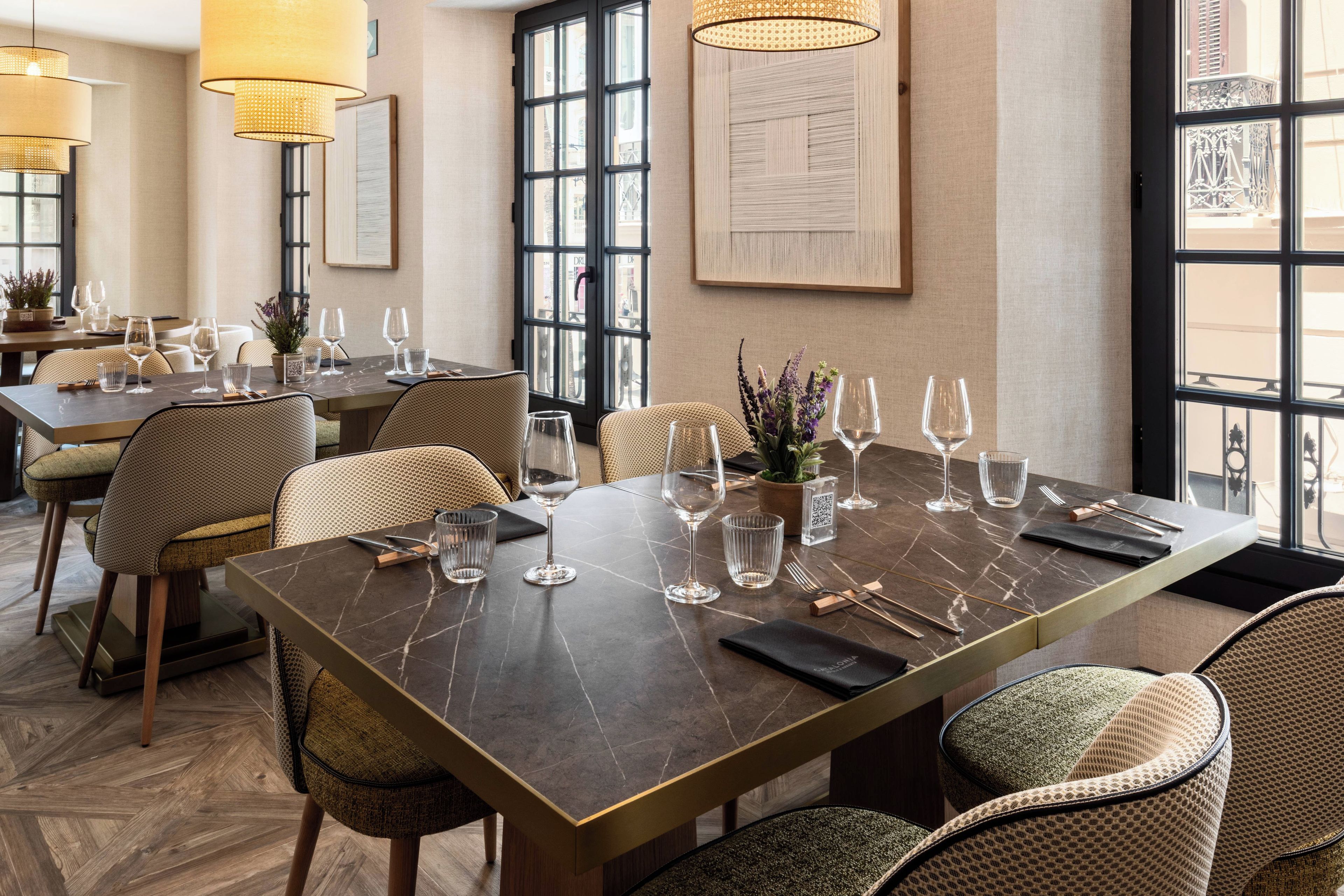 Un restaurant doté d’une longue table à manger, de nombreuses chaises et offrant une vue sur la rue grâce à de grandes fenêtres.